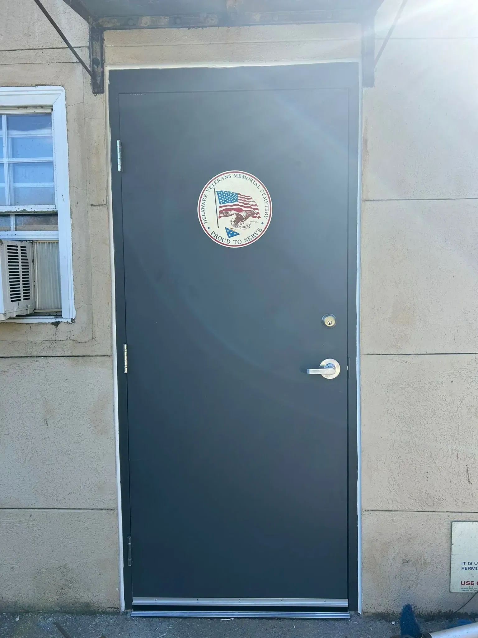 Dark gray door with a circular sticker, next to a weathered window, set in a light-colored building exterior.