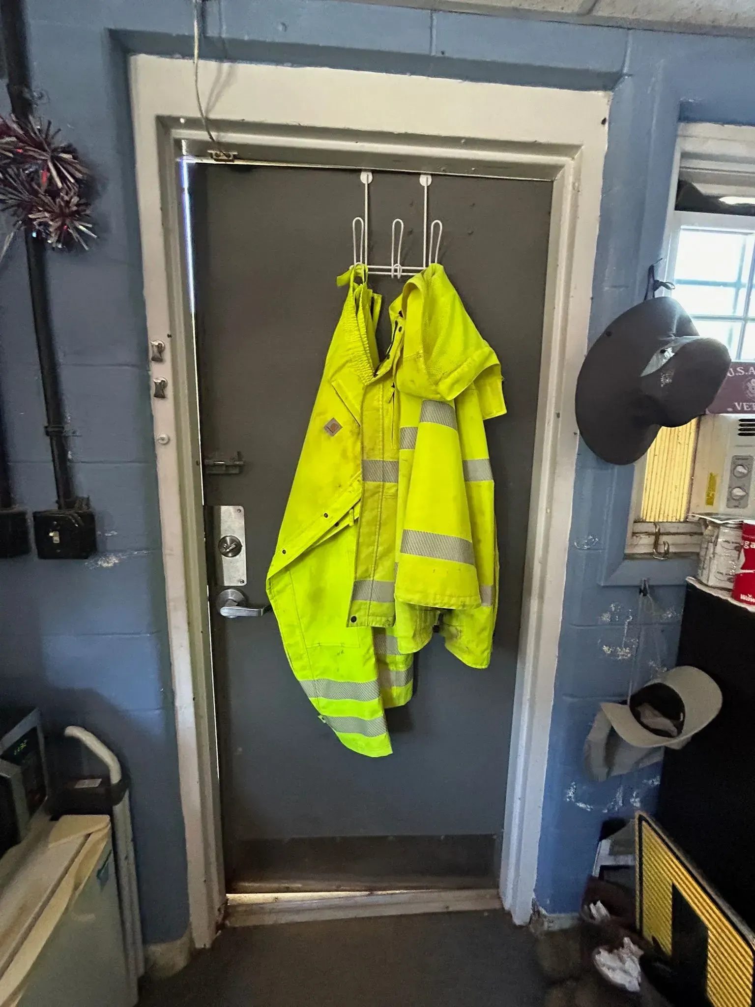 Bright yellow safety vest hanging on a door with a metal frame. Dark grey door.
