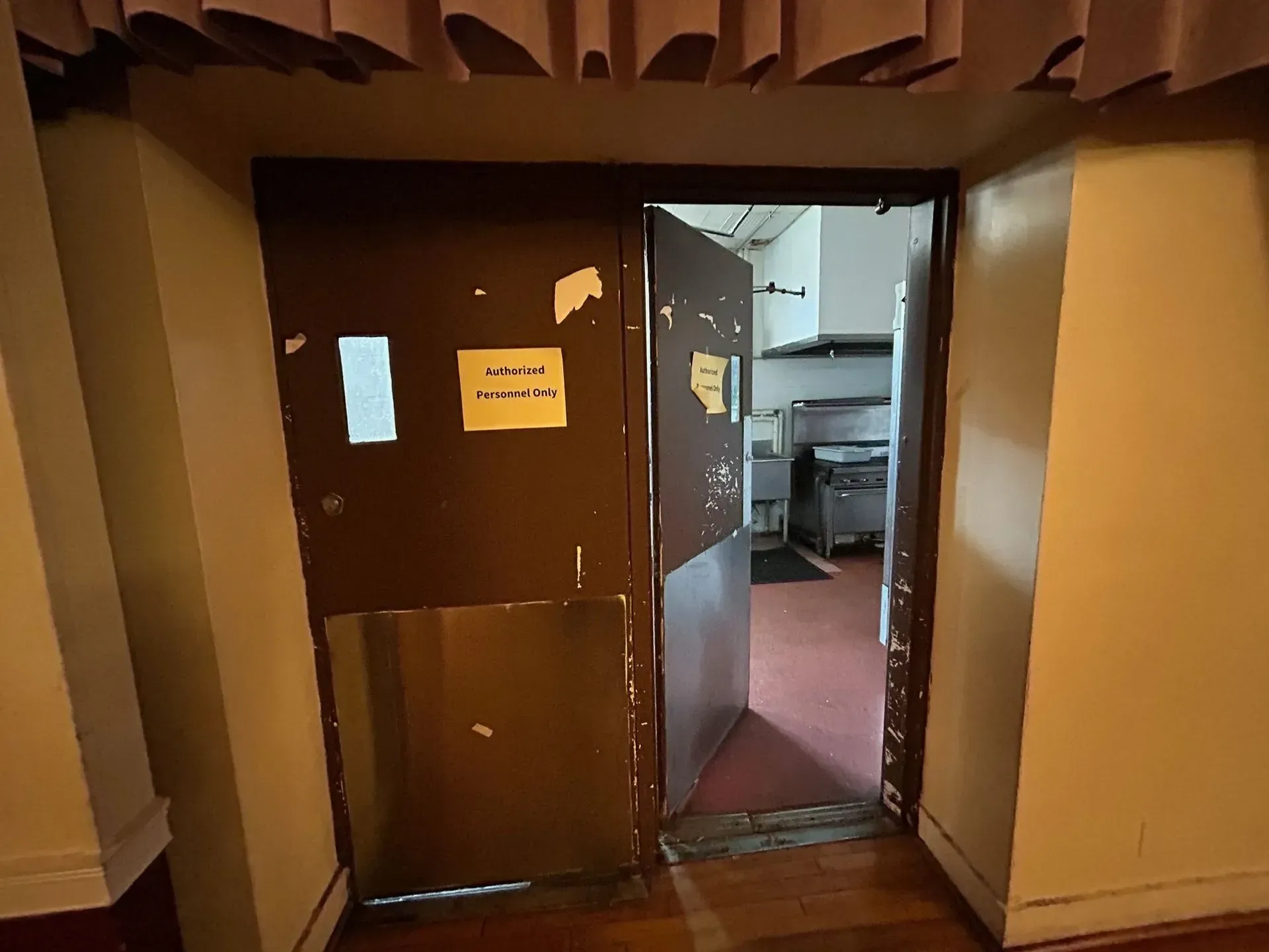 Brown double doors open into a kitchen with stainless steel appliances and a red floor.