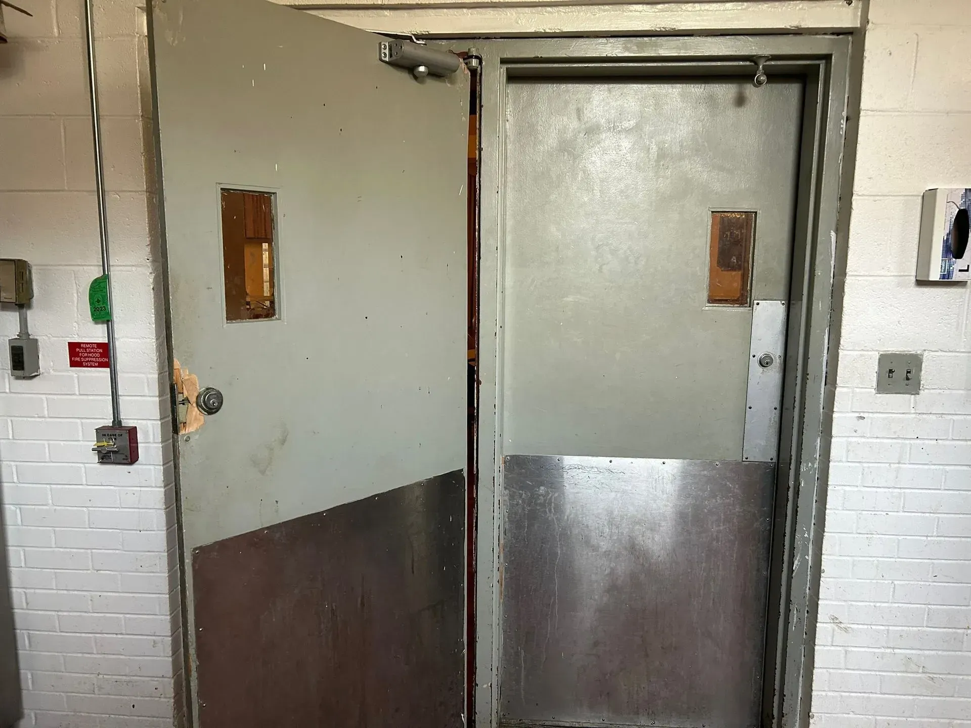 Gray and brown industrial double doors, one ajar, in a tiled hallway.