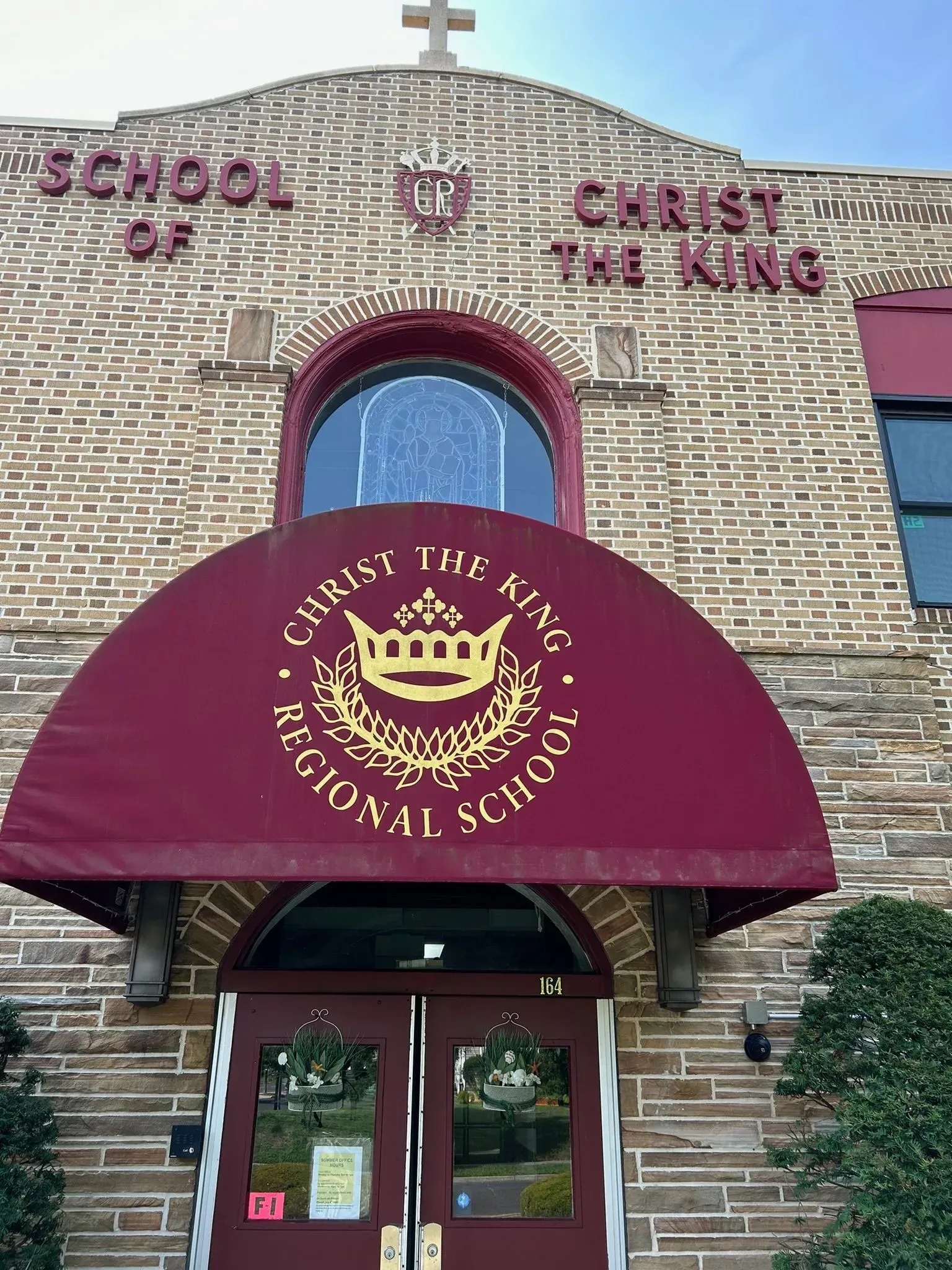 Christ the King Regional School entrance with burgundy awning, arched window, and brick facade.