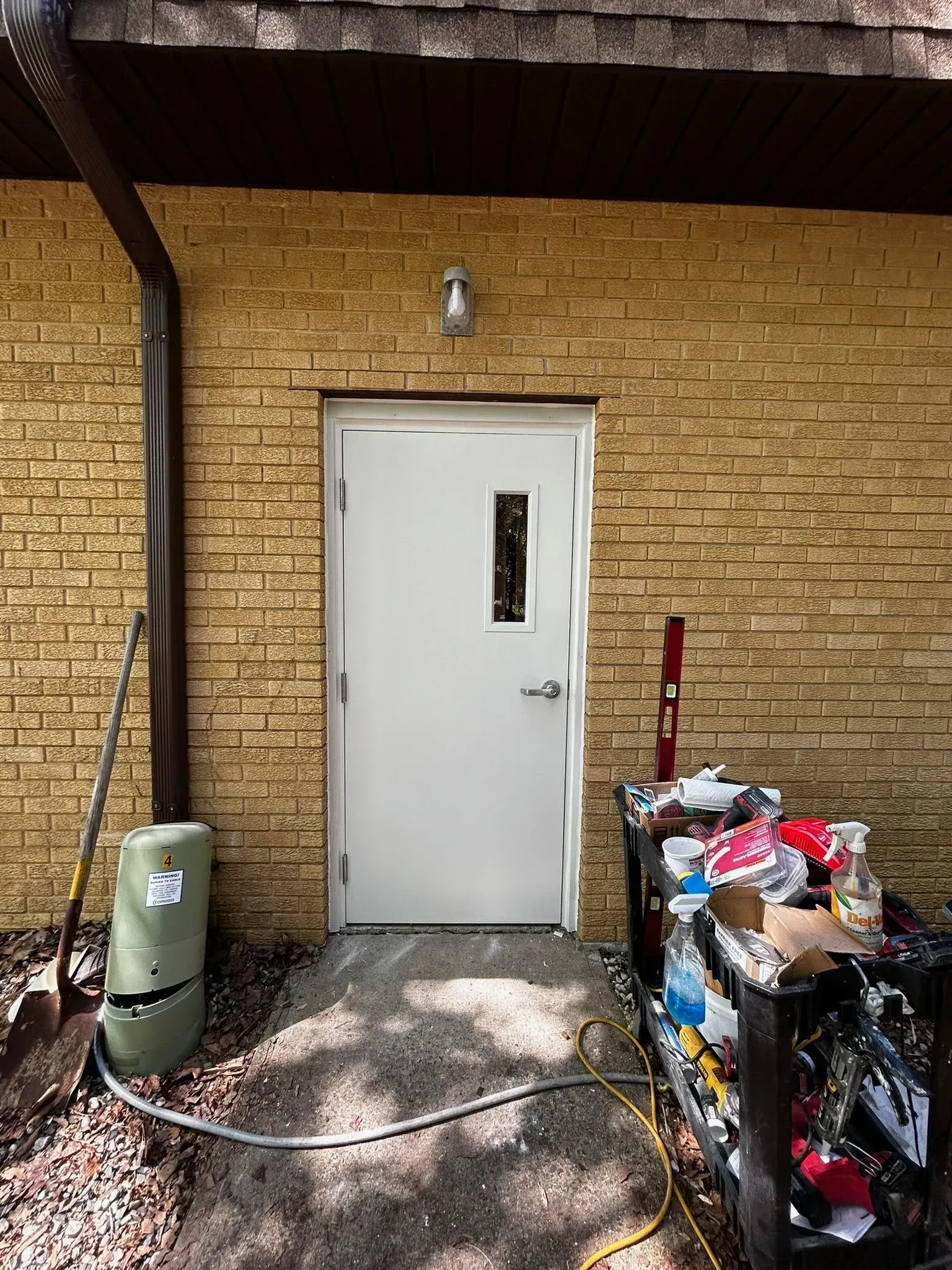 White door in brick wall with window, light above, and construction materials nearby.