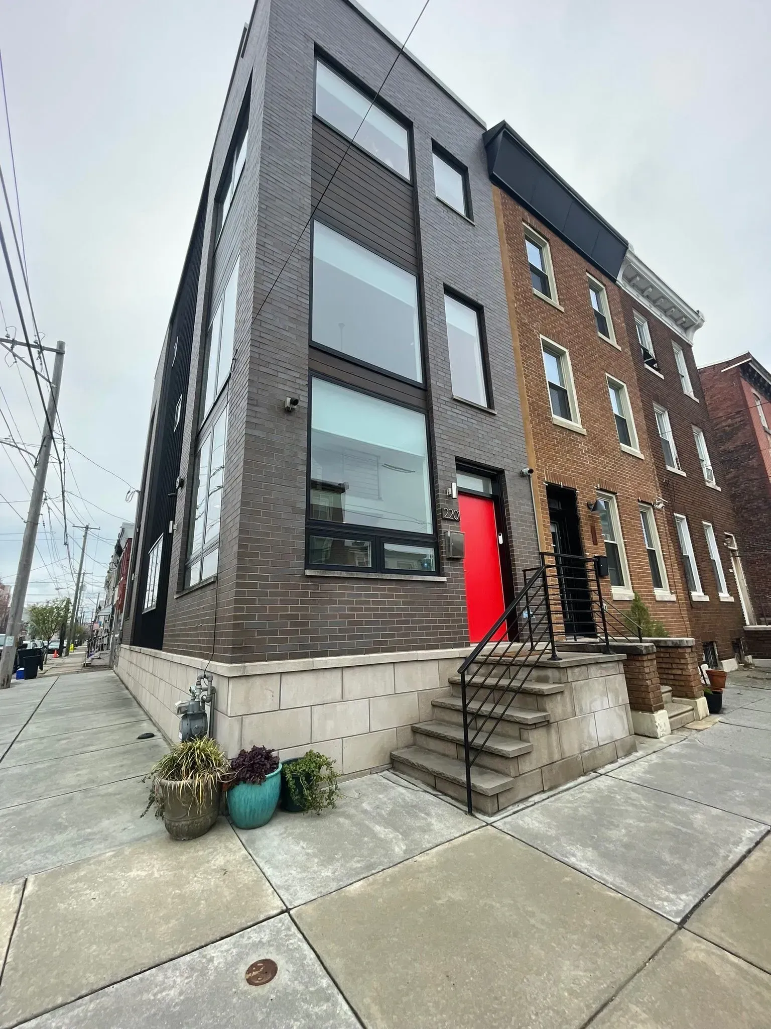Modern three-story building with red door next to a brick building; both on a city street.