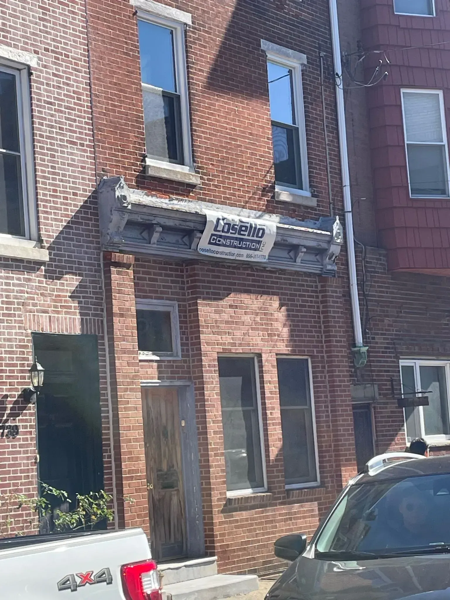 Brick building with multiple windows; a weathered wooden door; a sign says 