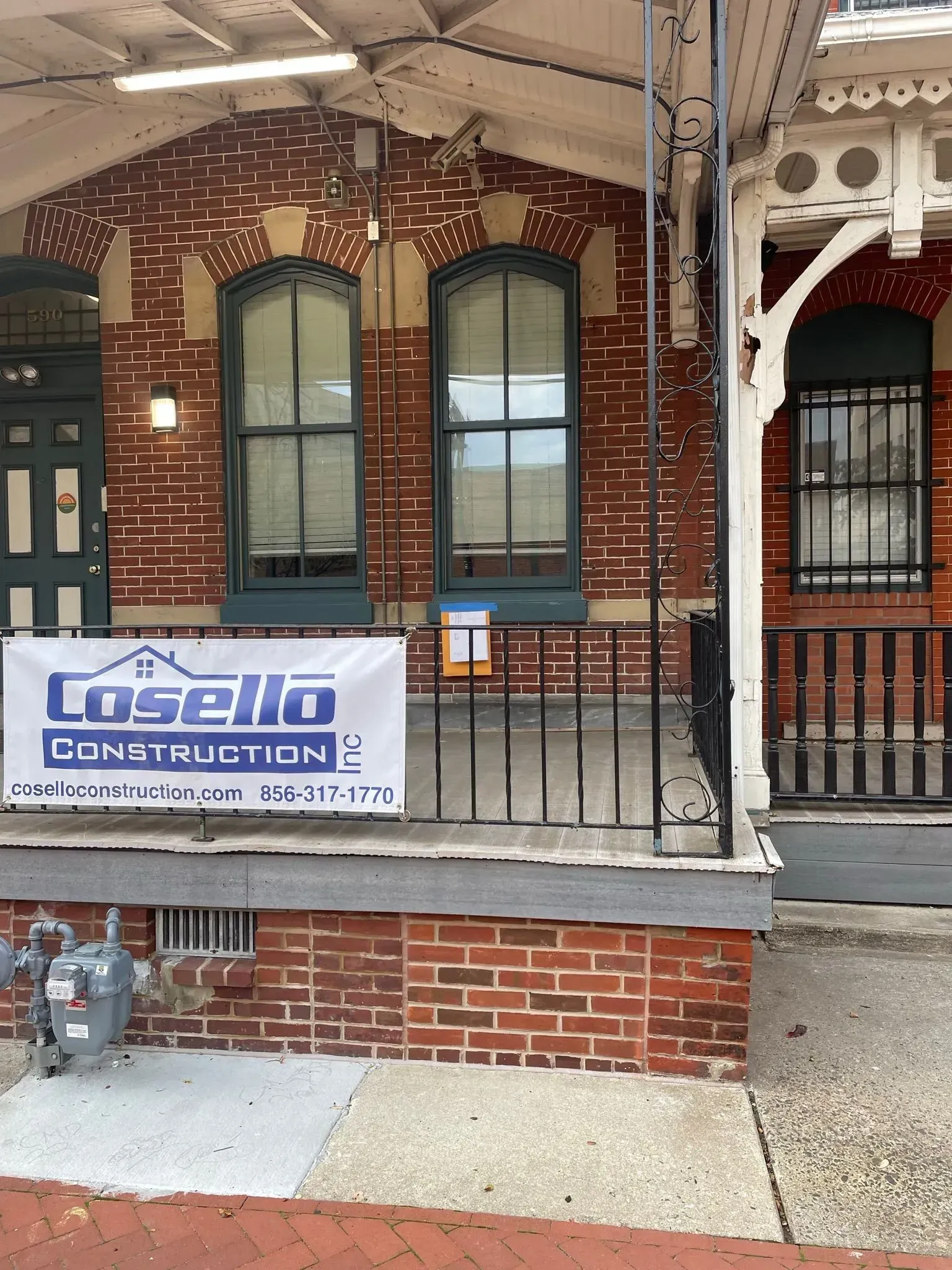 Brick building with Cosello Construction sign, two tall windows, and a small porch.