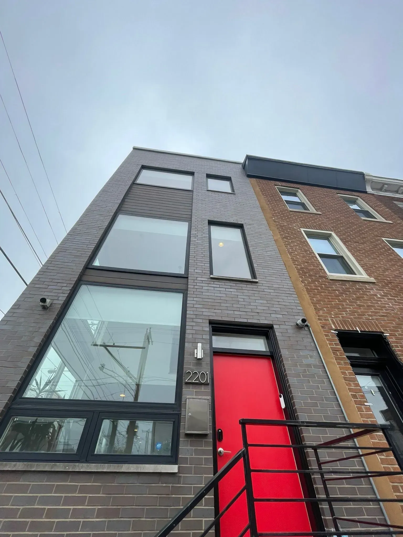 Modern brick townhouse with red door and large windows under a cloudy sky.