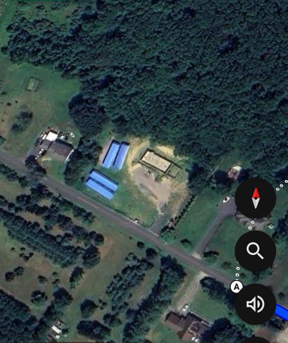 Aerial view of buildings with blue roofs and a road, surrounded by greenery.