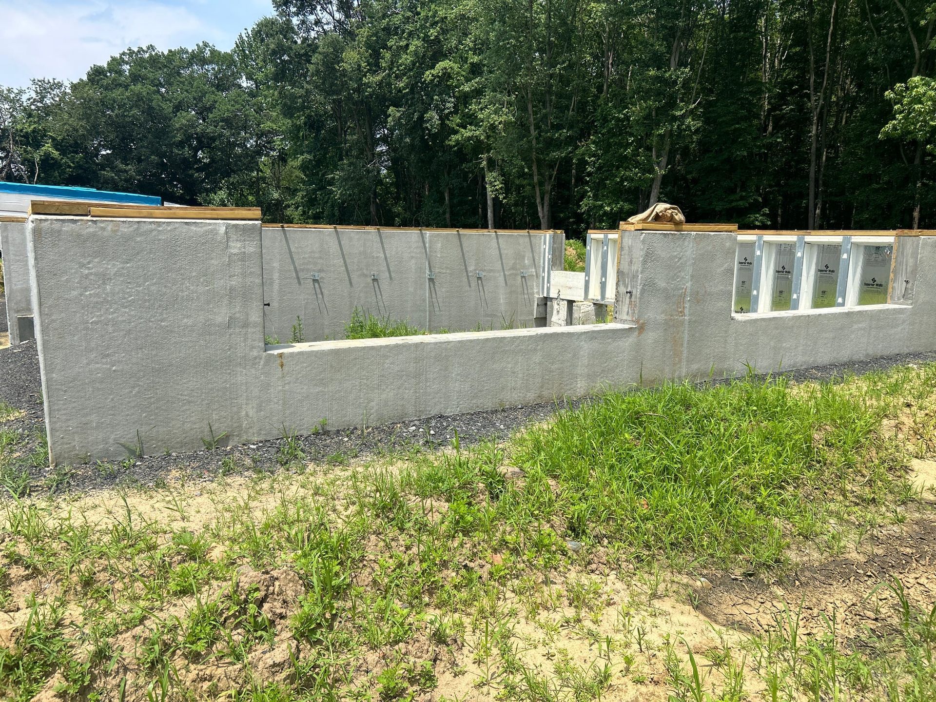 Concrete foundation walls with openings for windows and doors. Green grass and trees in the background.