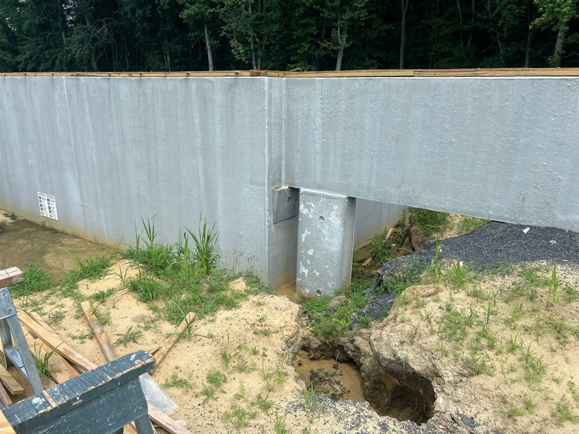 Concrete retaining wall with a gap, dirt ground, and some greenery.