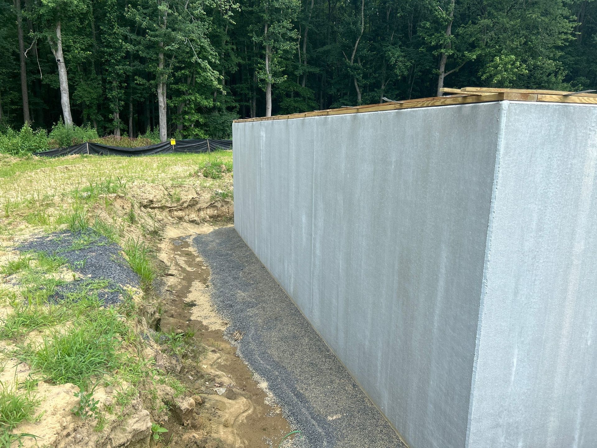 Concrete foundation wall with gravel drainage, grass and trees in background.