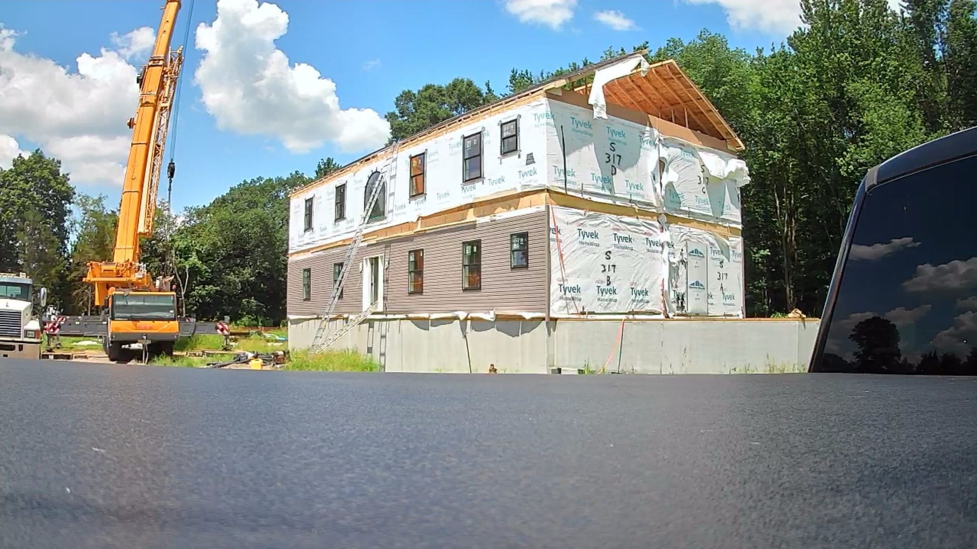 Construction site: Two-story building framed, covered in white wrap, and crane. Sunny day.