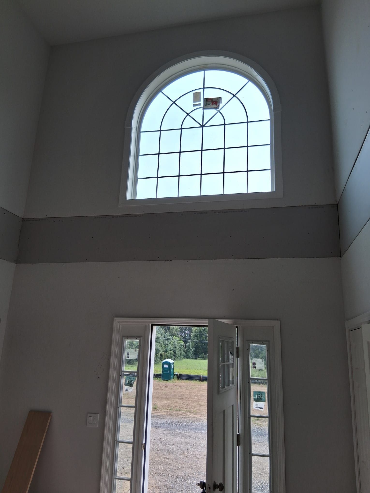 Interior view: arched window above a doorway. Gray walls, white trim, exterior view through the door.