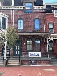Brick row house with arched windows, covered porch, and a business sign.