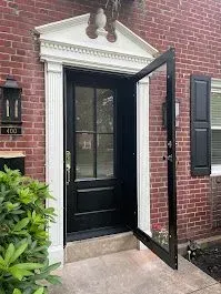 Black front door with open glass storm door in a red brick building.