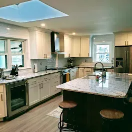 Kitchen with white cabinets, large island, stainless steel appliances, and skylight.