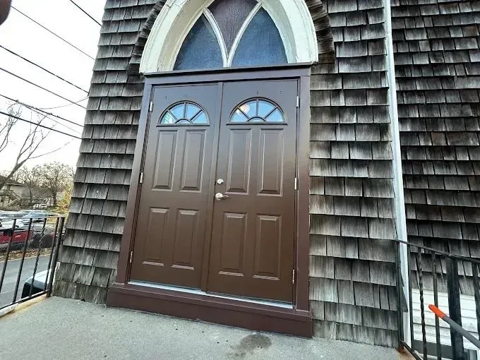 Brown double doors with arched window above, set in wood-shingled building facade.