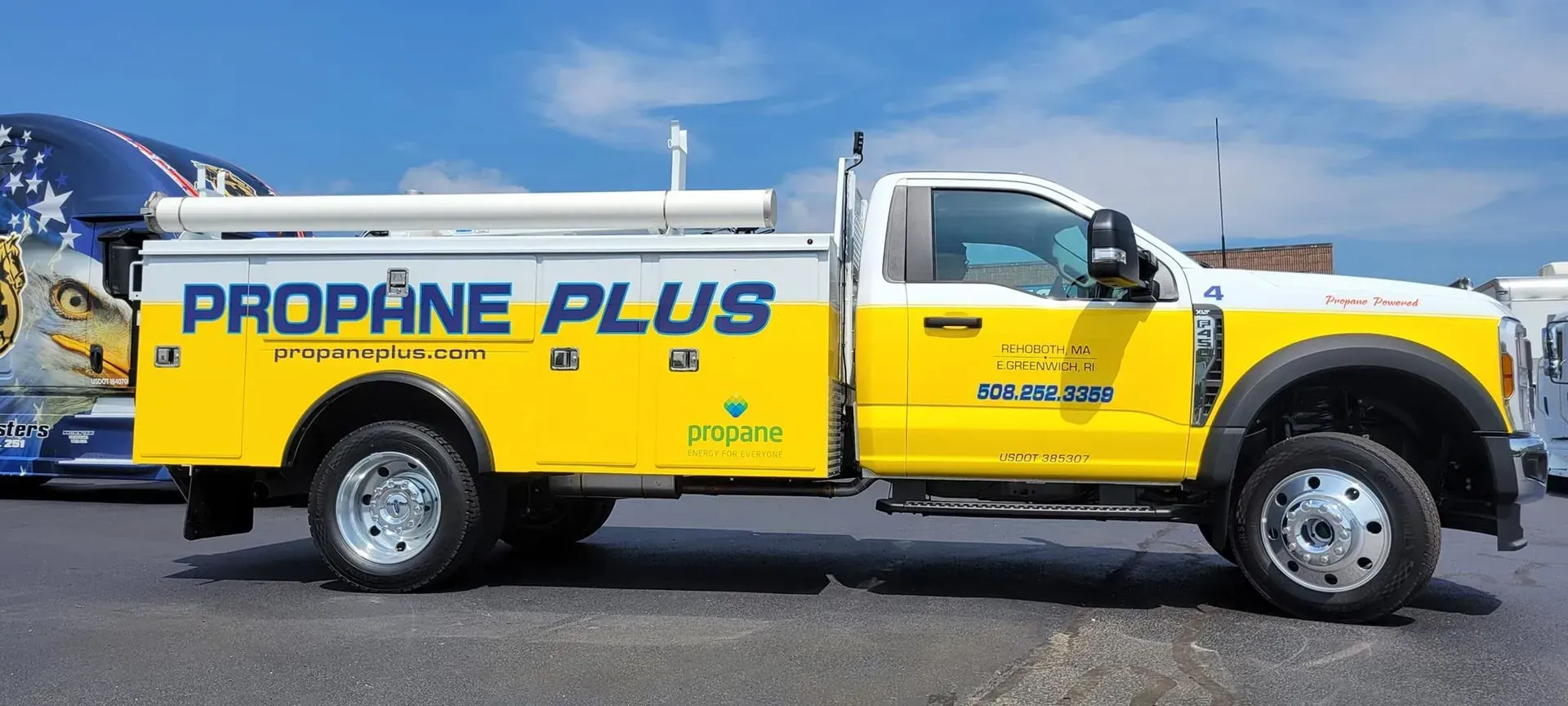 Yellow and white Propane Plus truck parked on asphalt under a blue sky.