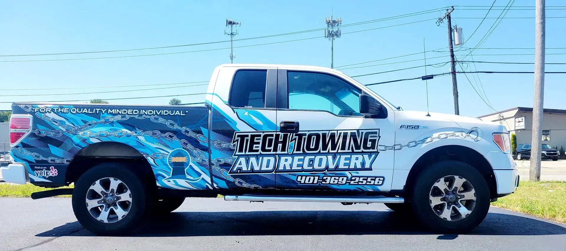 White tow truck with blue graphic on the side, parked on the street. 