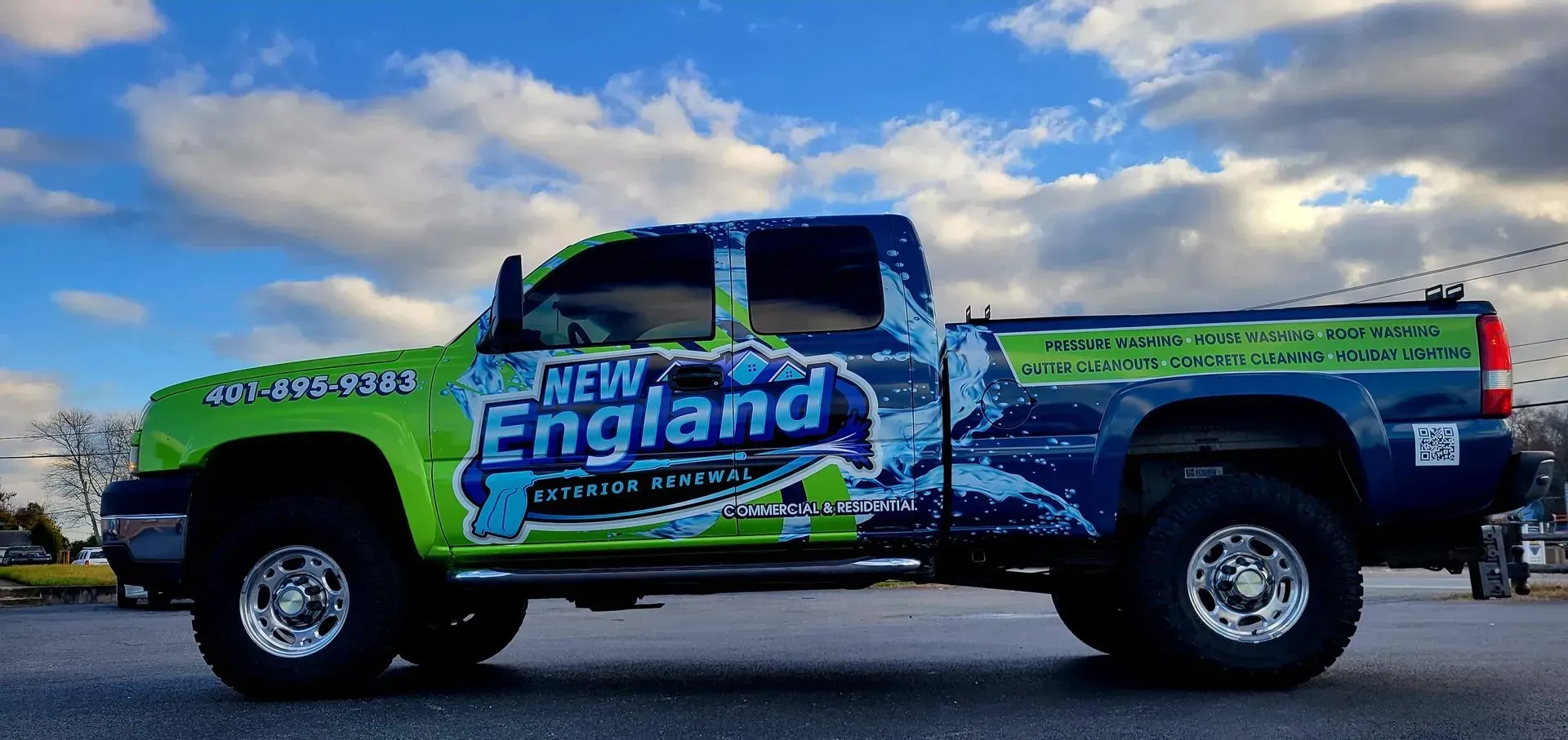 A green and blue New England custom systems truck parked outside with a cloudy sky background.