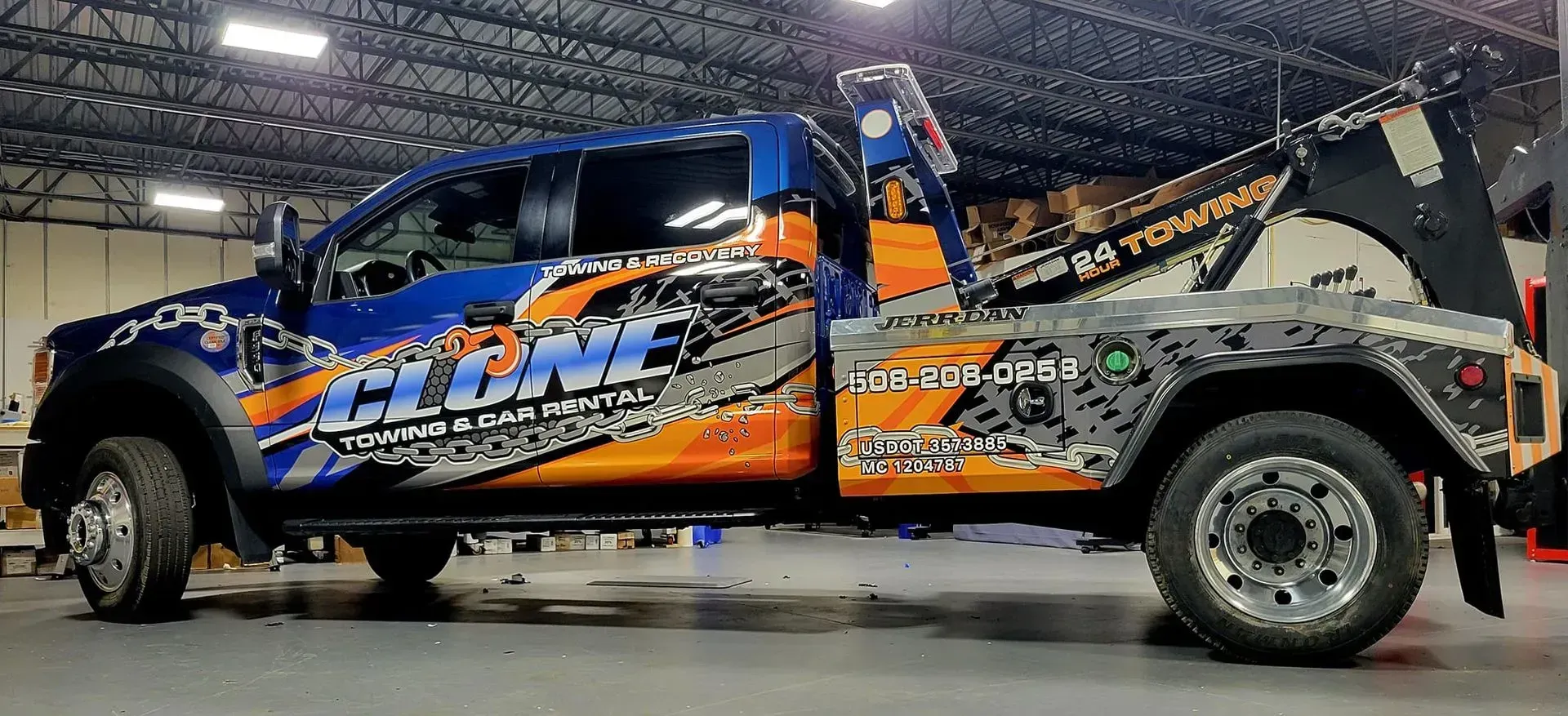 A tow truck with orange, blue, and gray graphics. It's parked in a warehouse.