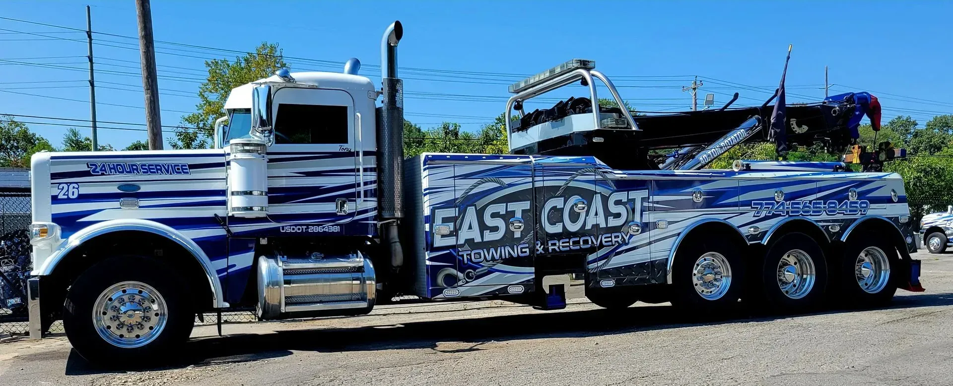A white and blue East Coast Towing truck parked on a sunny day.