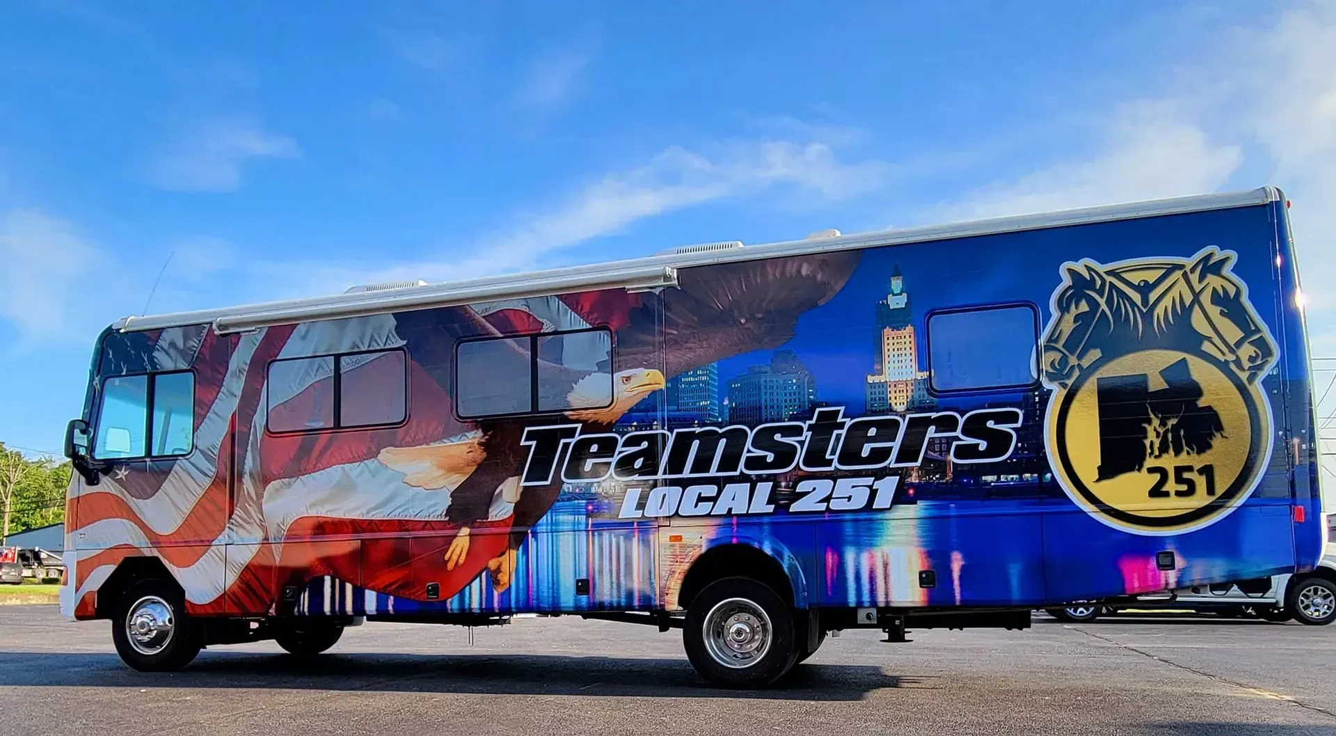 Teamsters Local 251 bus with patriotic design: US flag, eagle, and city skyline. Blue and gold.