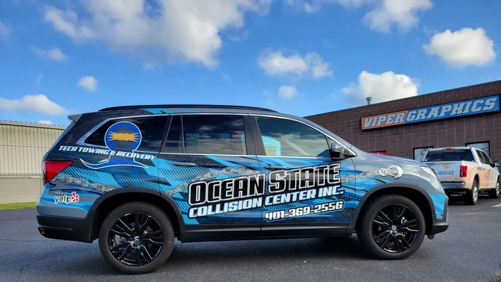 Blue and gray car wrap for Ocean State Collision Center, parked outside their building.
