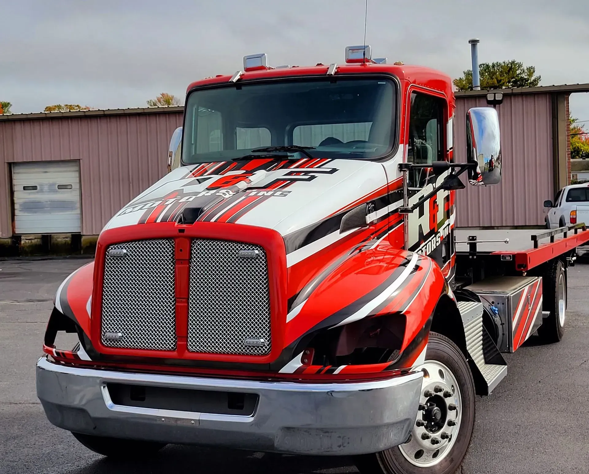Red and white tow truck with chrome accents parked in front of a building.