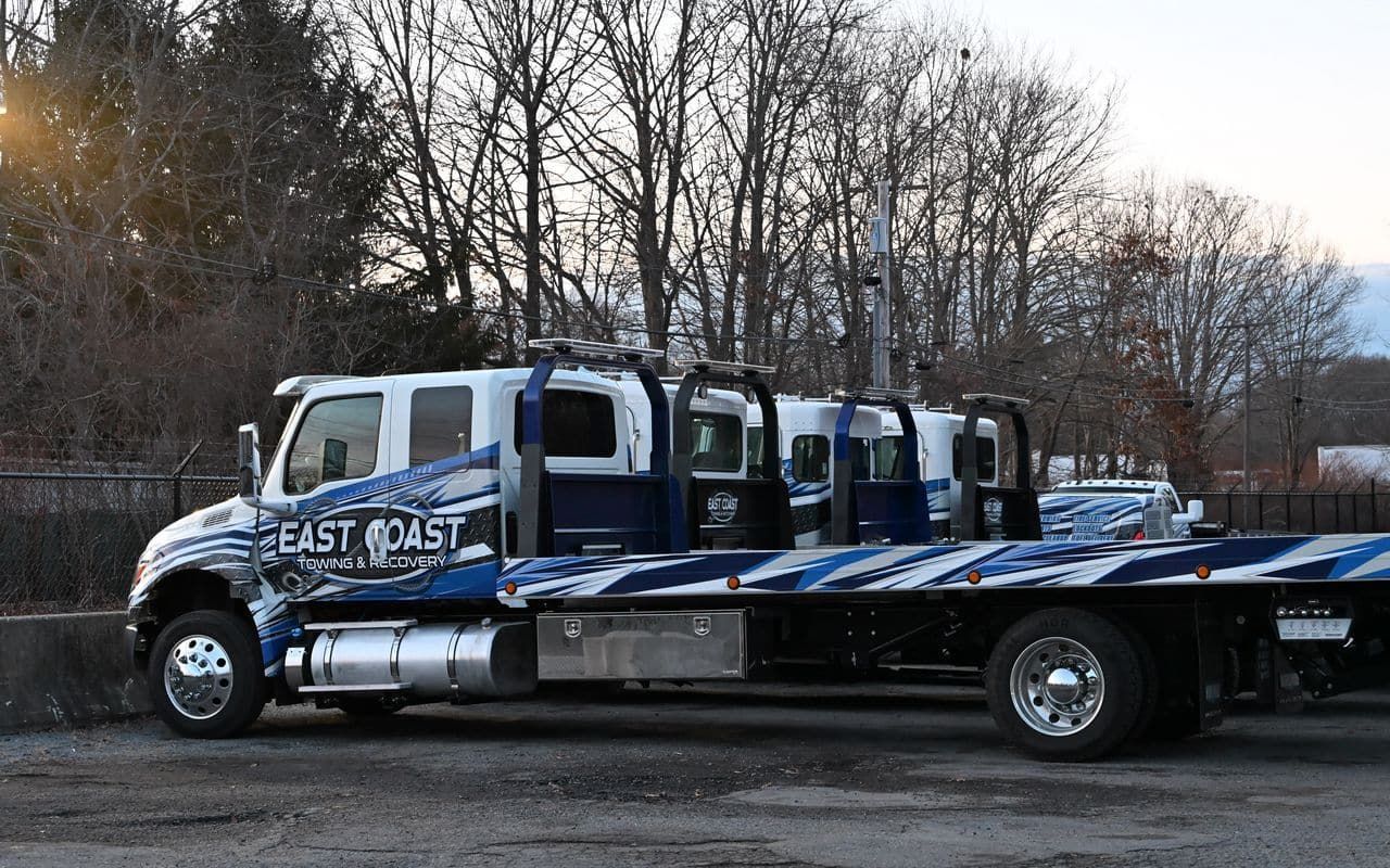 Tow truck with East Coast lettering; blue and white design; parked in lot.