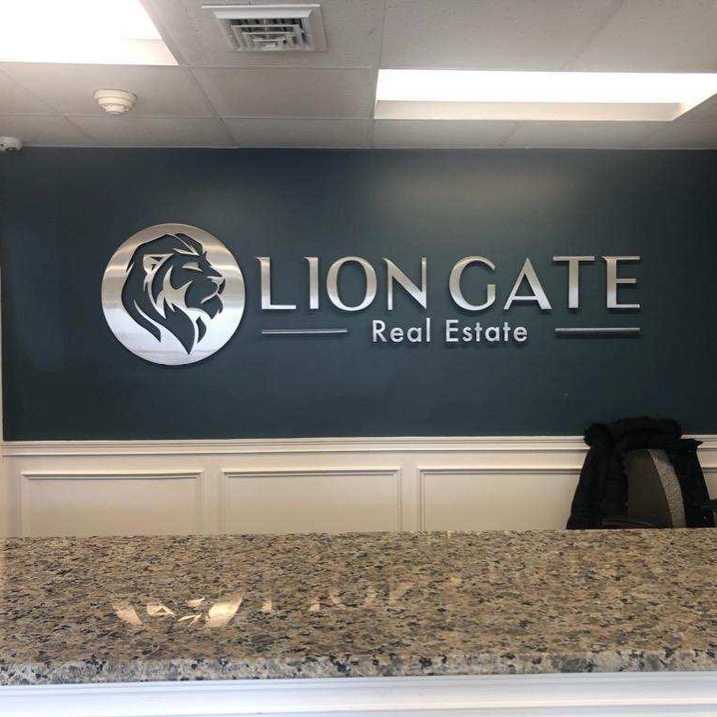 Lion Gate Real Estate office reception with a silver logo on a teal wall above a granite counter.