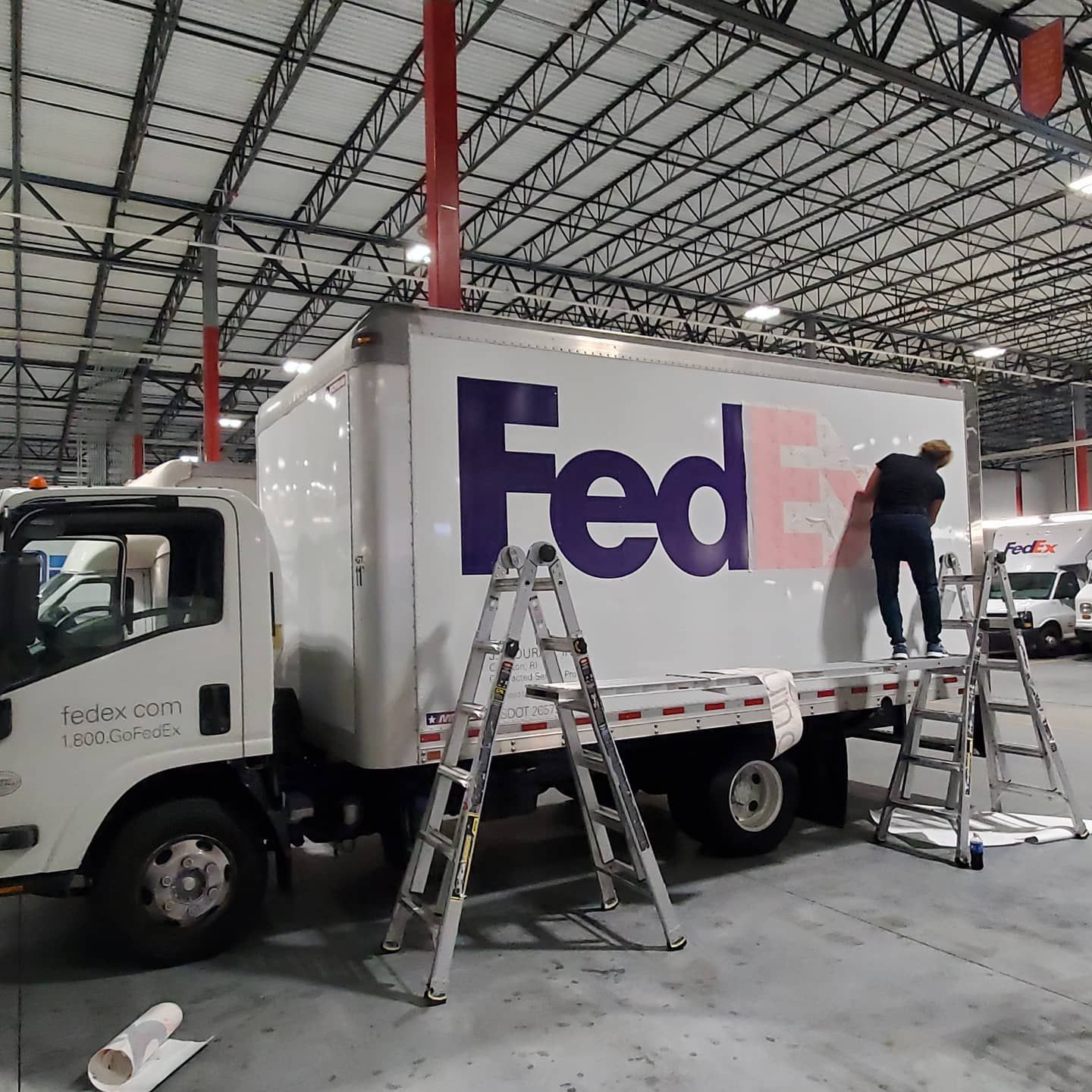 FedEx truck being worked on by a person on a ladder, indoors.