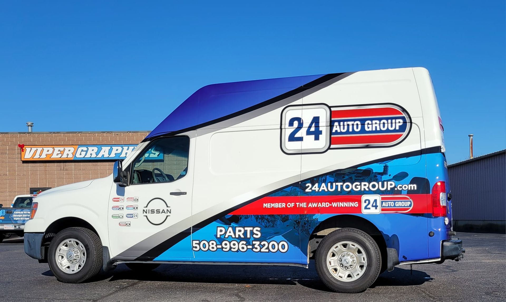 White Nissan van with blue and red graphics advertising 24 Auto Group.