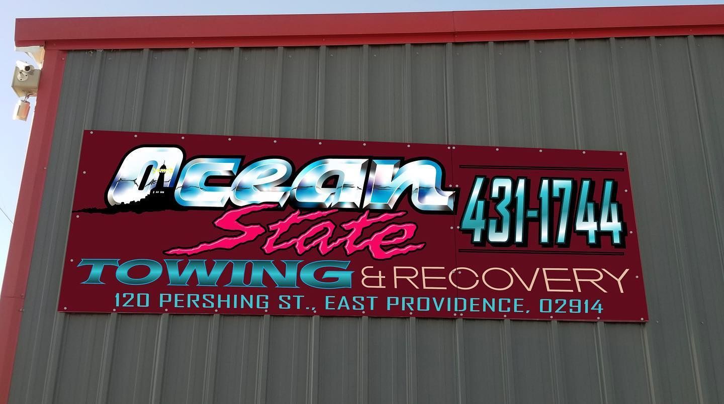 Sign for Ocean State Towing & Recovery, red and teal lettering, with phone number and address.