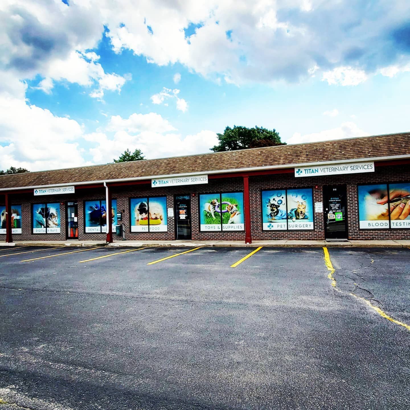A strip mall with several store fronts under a blue sky. Parking lot in front.