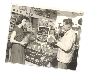 A black and white photo of a man talking to a woman in front of a sign that says hart 's quality lawn seeds