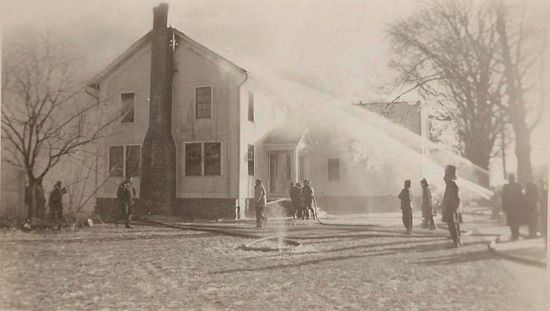 A group of people are spraying water on a fire in front of a house.