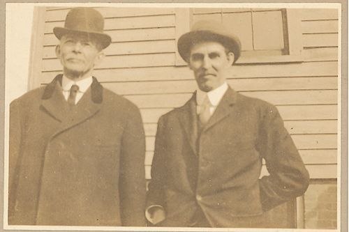 Two men in suits and hats are standing next to each other in front of a building.