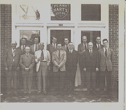 A group of men standing in front of a building that says plant hart 's seeds
