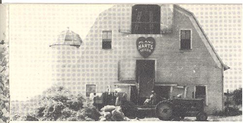 A black and white photo of a barn with a tractor parked in front of it