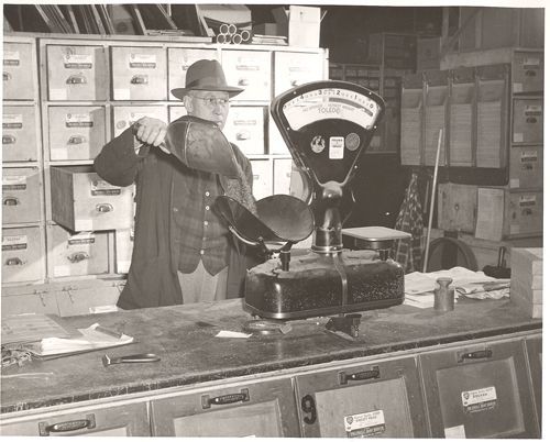 A black and white photo of a man standing in front of a scale