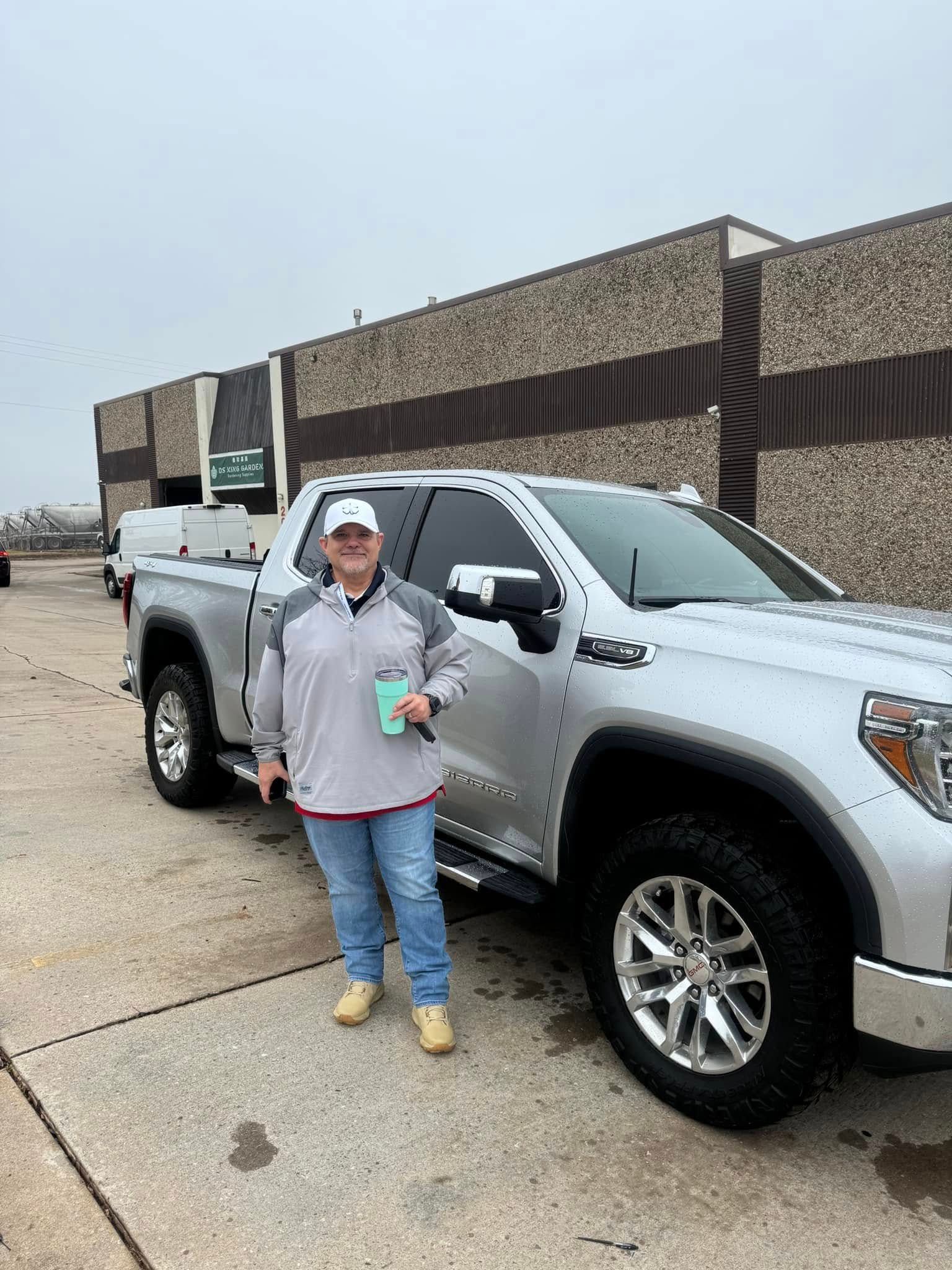 A woman is standing in front of a silver truck.
