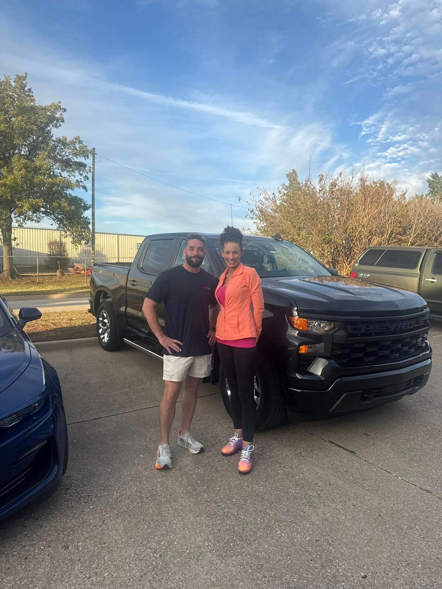 A man and a woman are standing in front of a black truck.