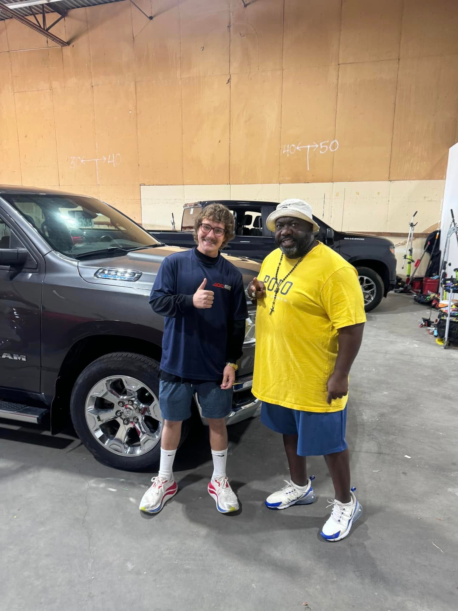 Two men are standing next to a truck in a garage.