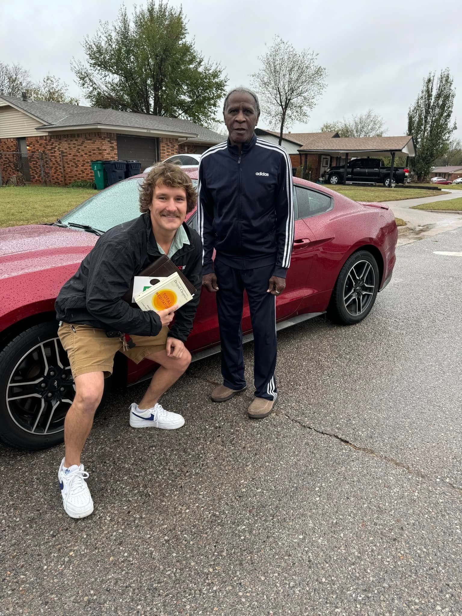 Two people are posing for a picture in front of a red car.