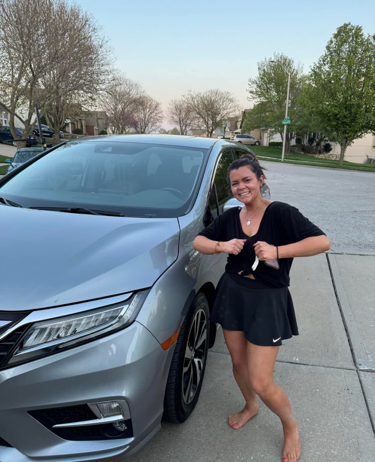 A woman is standing in front of a silver car.