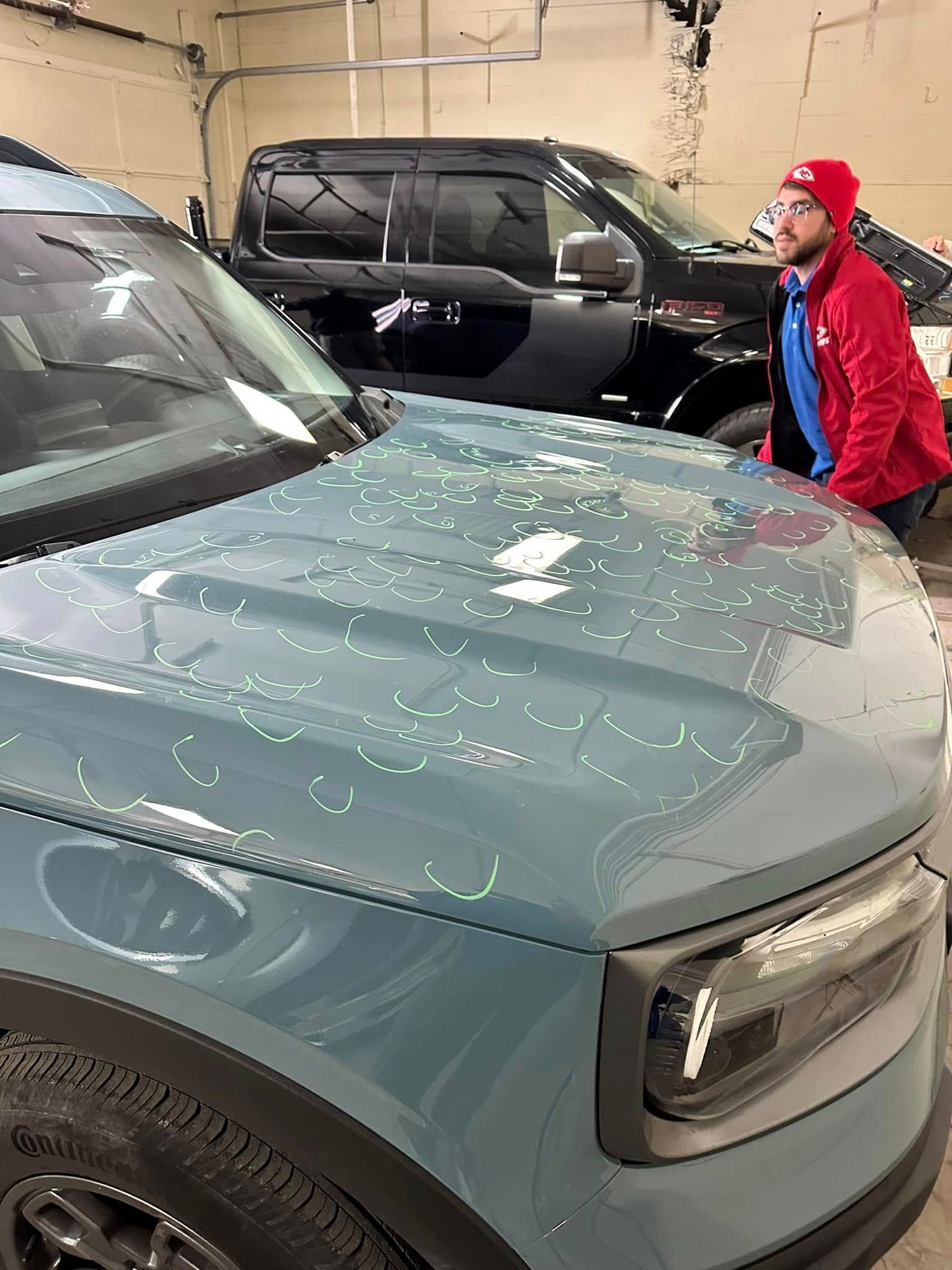 A man is standing next to a blue car in a garage.