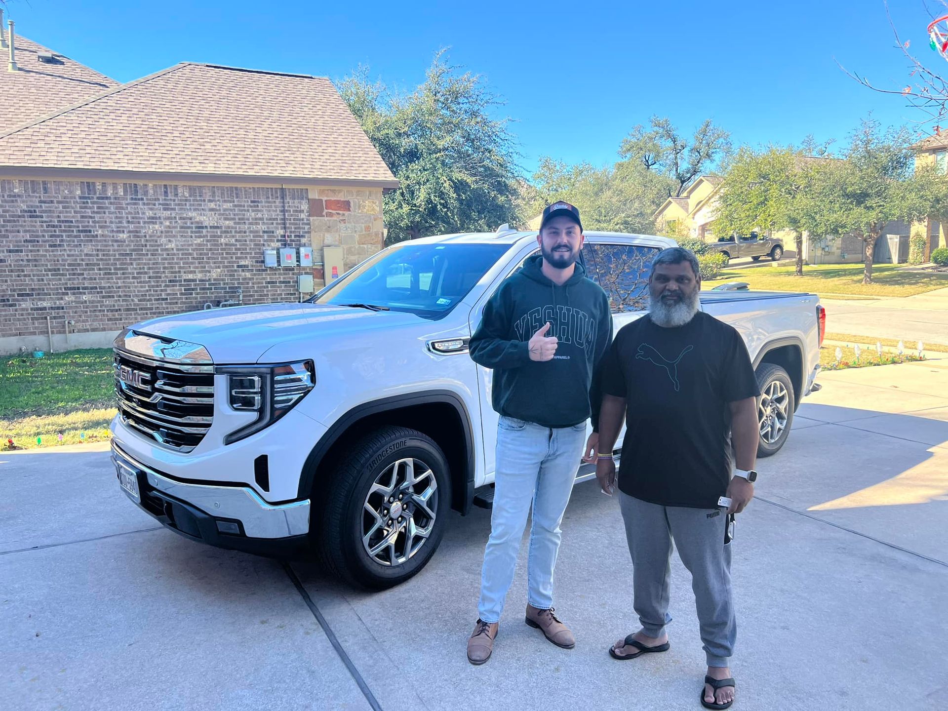 Two men are standing next to a white truck in a driveway.