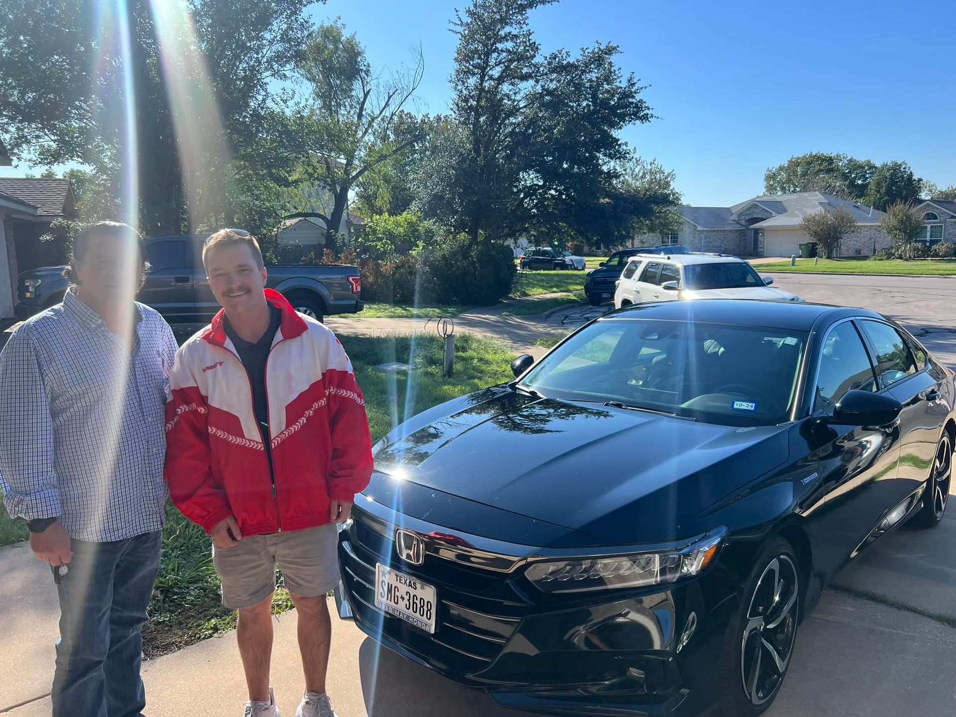 Two men are standing next to a black car in a driveway.
