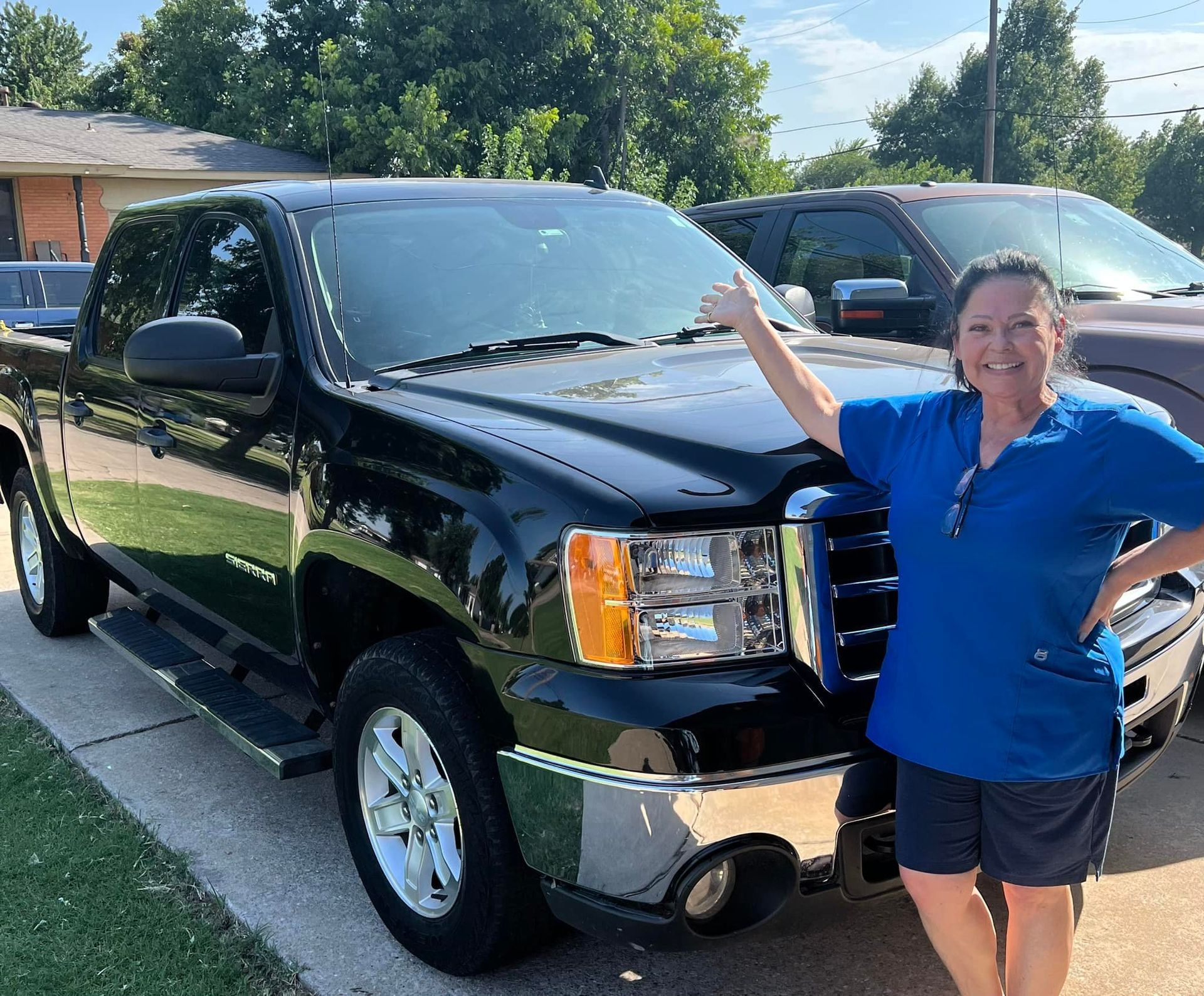 A woman in a blue shirt is standing next to a black truck.