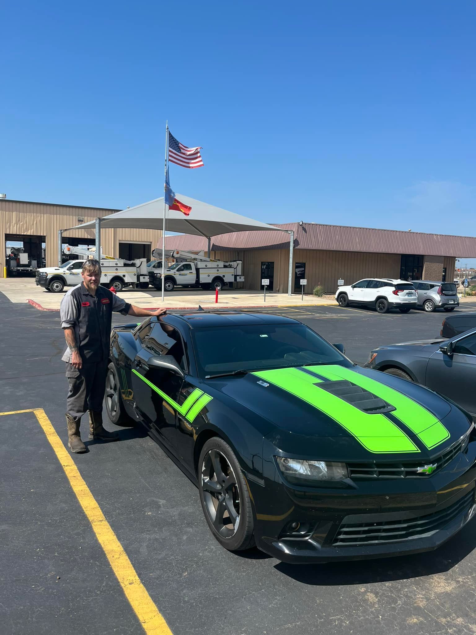 A man is standing next to a black car with green stripes in a parking lot.